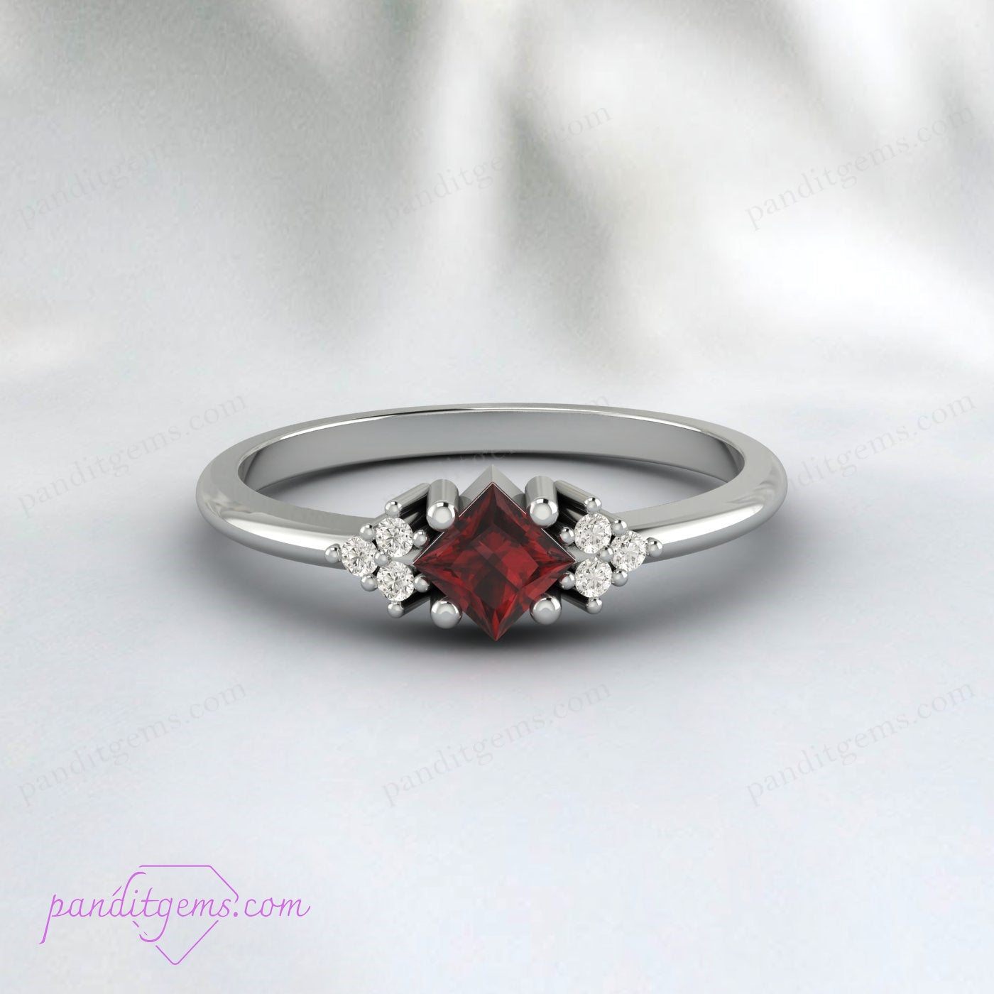 Close-up of a deep red garnet ring with trio diamond accents, perfect for engagements or anniversaries.